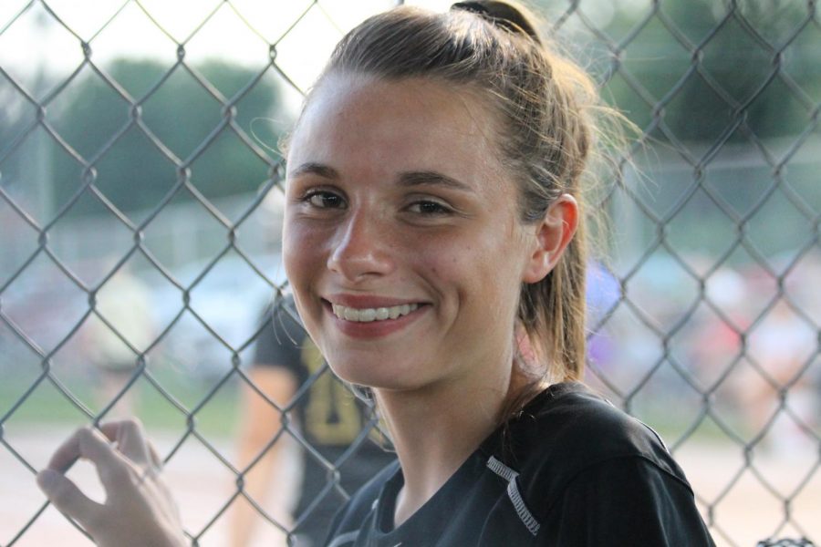 Mackenzie standing in the dugout supporting her teammates bat. 