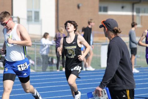 Reid Simmons (9) running in the 1600m event while being encouraged by Coach Garrity.