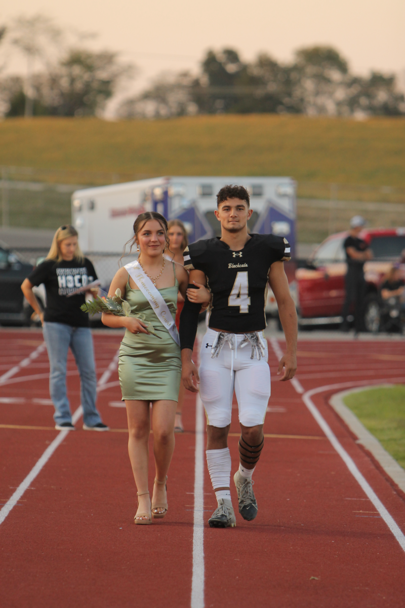 Couple Ava Hovis and DJ Baca walking side by side and their families cheer them on. 