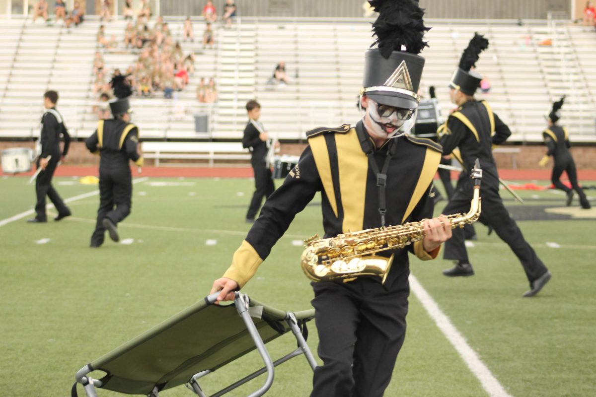 Ethan Vance (12) moves props off the field during the change of songs, as his band members run around frantically in the back.